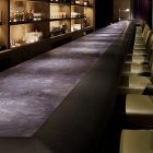 日比谷ミッドタウンスターバーのモールテックスのバーカウンター、右手前には照明があり、左手前には椅子が並び、奥の棚には酒瓶やグラスが並んでいる 日比谷ミッドタウンスターバーのモールテックスのバーカウンター、右手前には照明があり、左手前には椅子が並び、奥の棚には酒瓶やグラスが並んでいる
