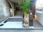 大阪都会の玄関まわりエクステリアリフォームが完成しましたモルタルと黒いタイルで仕上げた土間白いアルミ柱で作った門柱は樹脂木パネルで表札とインターホンポストを取付けました。シンボルツリーのあるすっきりしたエクステリアとなりました