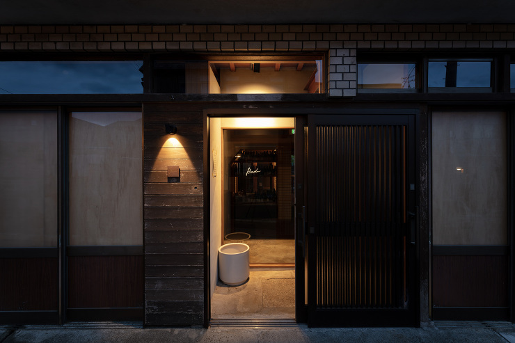 京都の町家を改装したレストランBaduの外観。木とレンガのファサードに柔らかな灯りがともる。柳原照弘氏のデザイン監修のもと洛（RAKU）が施工を担当。