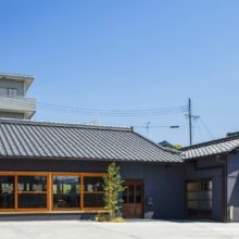 外観（正面）<br />
・屋根瓦を強調する意匠とするため、外壁はダークグレーの吹付塗装を施した。吹付塗料は、弾性系で揺れに追従。加えて防水性もあるため、壁面の漏水対策にも効果を発揮。
