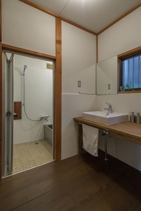 針葉樹合板の造作カウンターと洗面器だけのシンプルな洗面室。浴室はレトロな床タイルを尊重して再利用。壁面のみ防カビペイントで白く塗装。