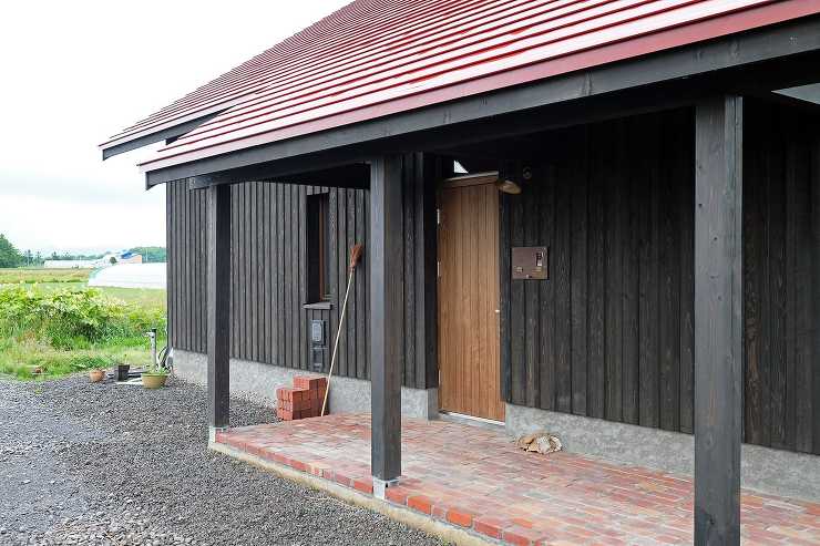 レンガ敷きの玄関ポーチと黒墨色の外壁板張りと赤い板金屋根