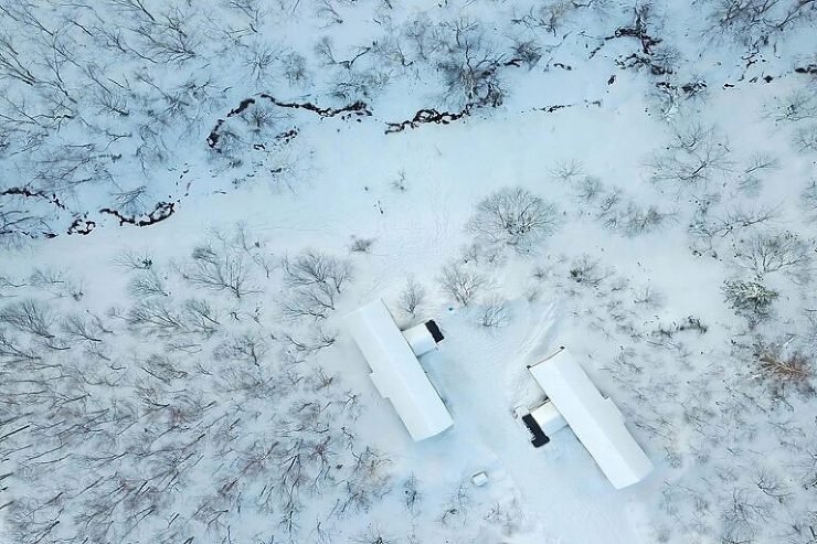 Aerial view of Sogetsu and Shakuzan, two minimalist homes nestled quietly within a dense forest, blending seamlessly with nature