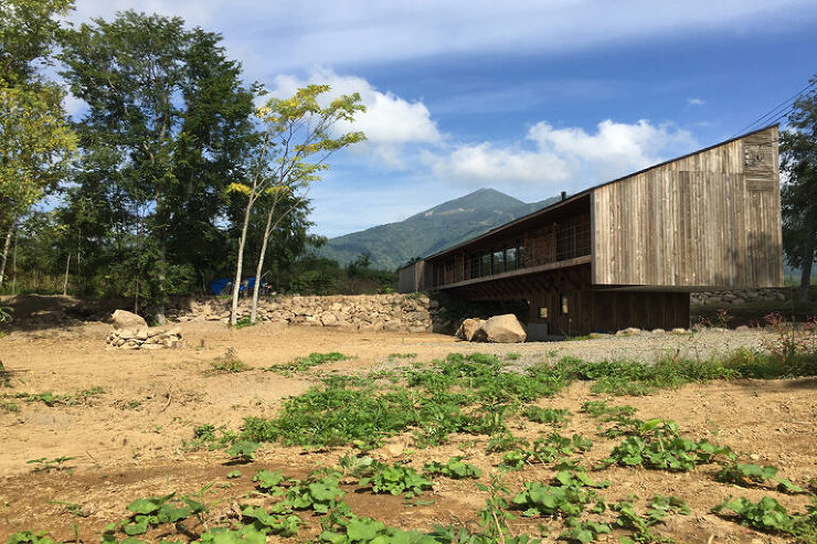 山の稜線に合わせた屋根形状と、ひな壇状の敷地にまたがる設計が特徴の建物。豪雪地域の特性を考慮し、雪の影響を軽減する工夫が施され、その土地の気候に寄り添ったデザインとなっている外観。