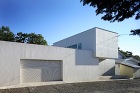 コンクリートの壁と二つの白い壁が異なる奥行きで交合う住宅